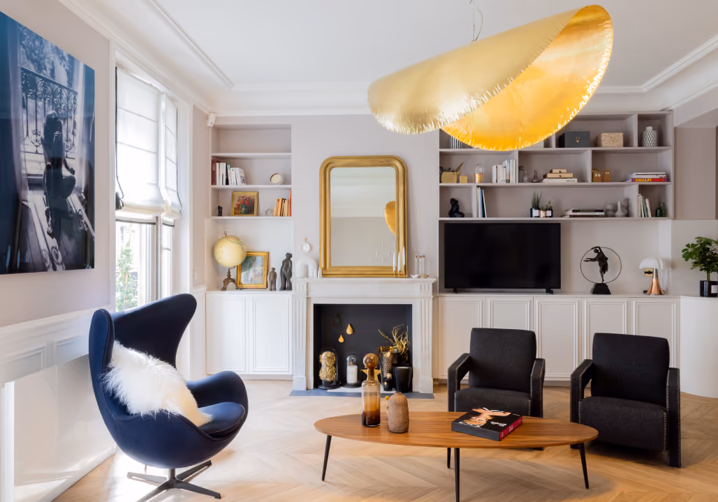 Modern living room with a blue egg chair, two black armchairs, wooden coffee table, and a large gold pendant light.