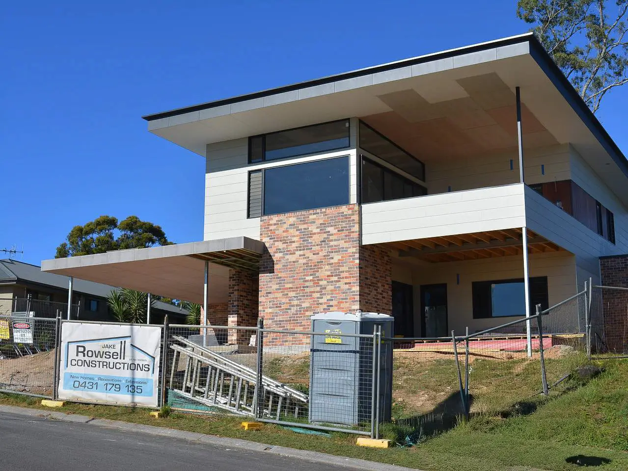 Modern two-story house under construction with brick and white panel exterior and fenced yard.