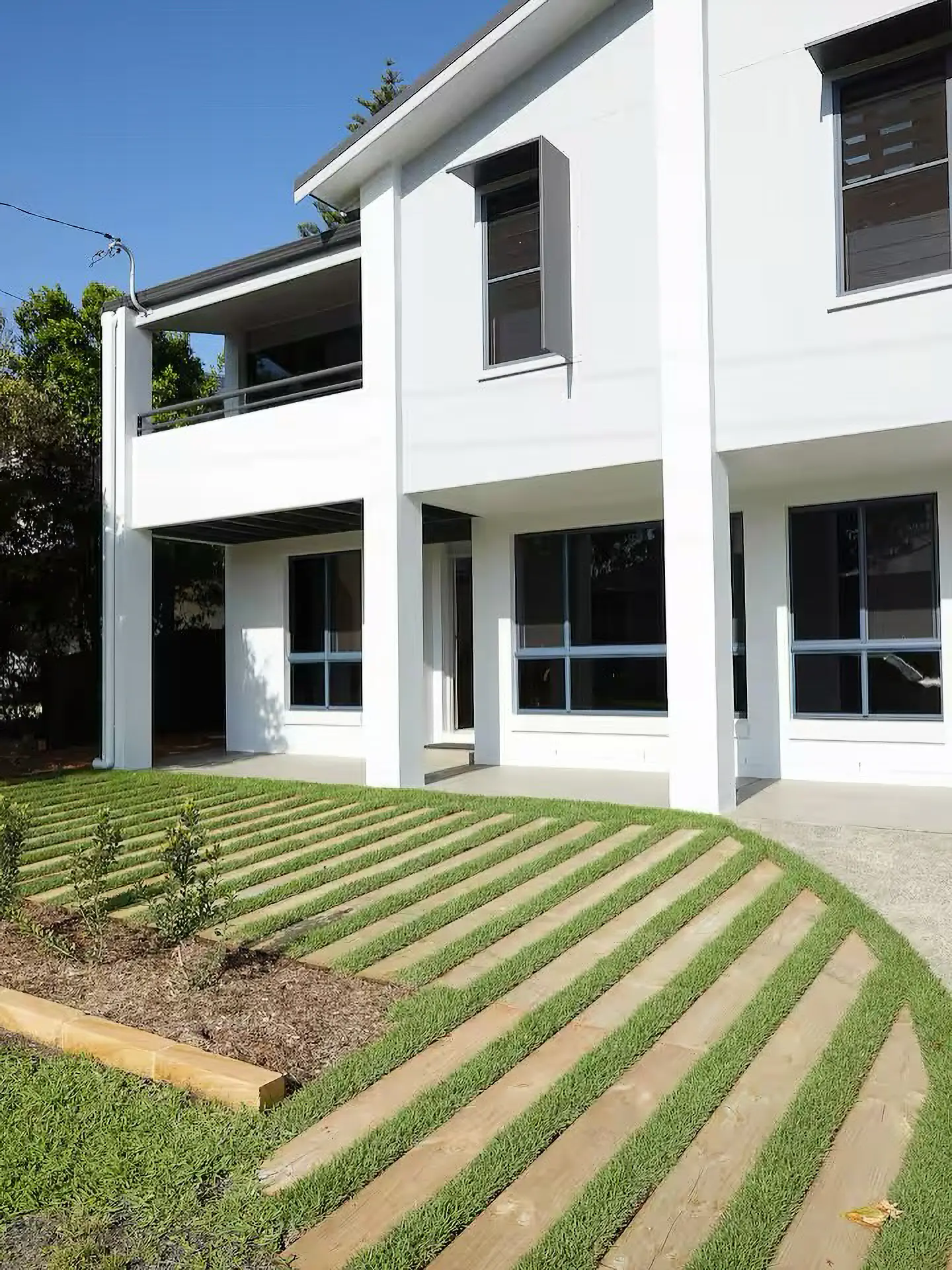 White modern house with large windows and front yard featuring wooden slats with grass strips.