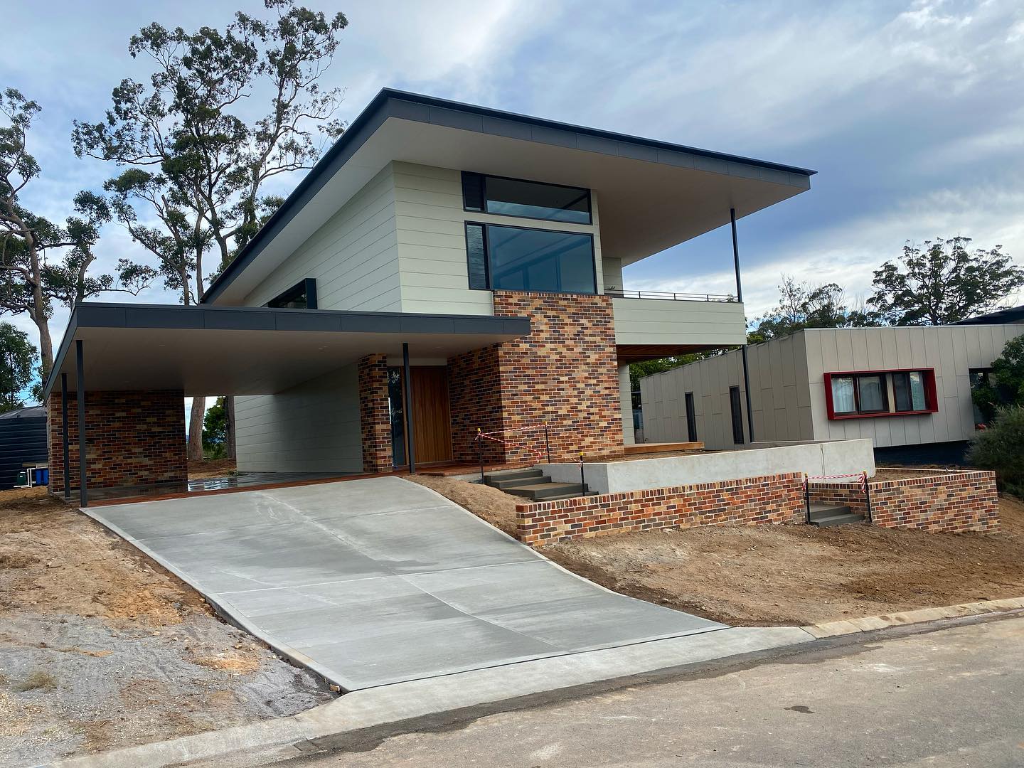 Modern two-story house with brick and light siding, a large driveway, and a flat roof carport.