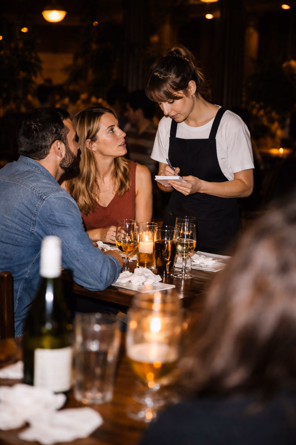 Waitress taking order from a couple seated at a candlelit restaurant table with drinks.