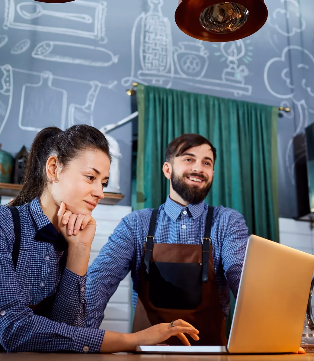 Two restaurant staff reviewing tip reports on a laptop behind the counter.