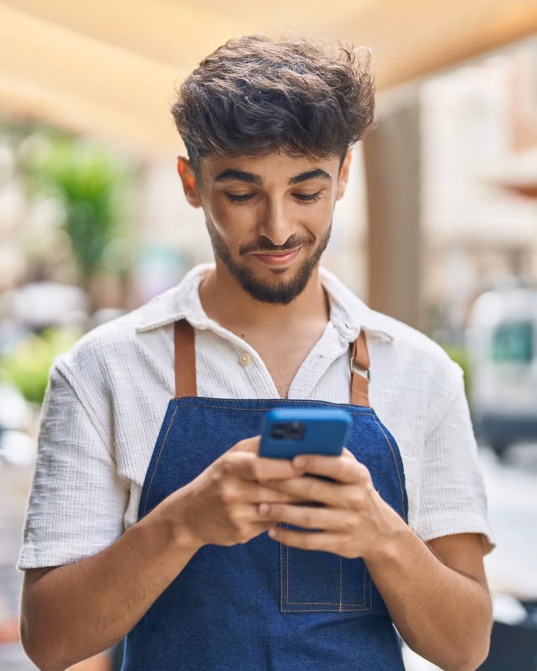 Restaurant worker in an apron checking his tips on his phone.