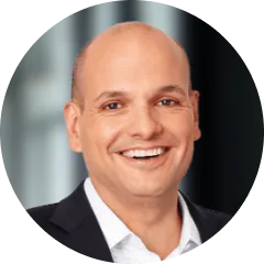 Smiling bald man wearing a dark suit and white shirt in a professional headshot.