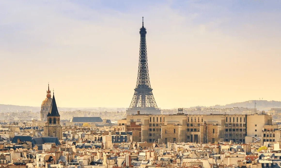 View of the Eiffel Tower rising above Paris rooftops at sunset with a clear sky.