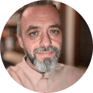 Portrait of a middle-aged man with a salt-and-pepper beard and mustache, wearing a light pink collared shirt.