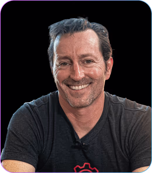 Smiling man with short dark hair wearing a black t-shirt against a black background.
