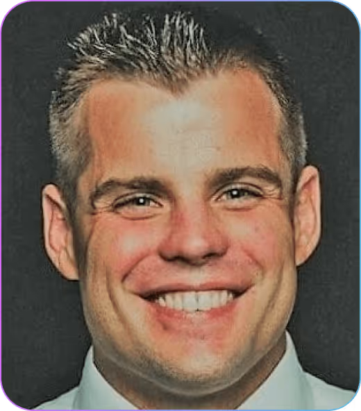 Smiling man with short spiked hair wearing a white shirt against a dark background.