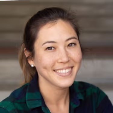 Smiling woman with dark hair tied back wearing a green and navy plaid shirt.