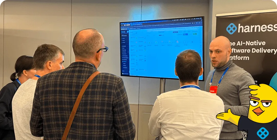 Five people attend a software presentation with a screen displaying a platform interface and a banner for Harness.