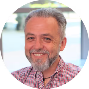 Smiling middle-aged man with gray hair and beard wearing a red checkered shirt.
