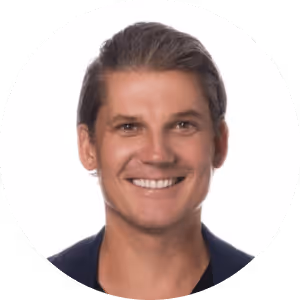 Smiling man with light brown hair styled back wearing a dark blazer.