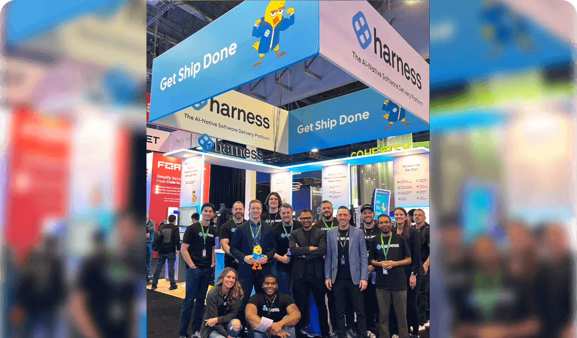 Group of smiling people posing at the Harness booth with blue and white banners reading 'Get Ship Done' at a tech conference.