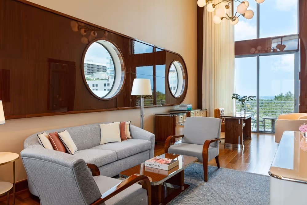 Sala de estar com dois sofás cinzas, poltronas e uma janela redonda no Mr. C Miami – Coconut Grove, um hotel de luxo.