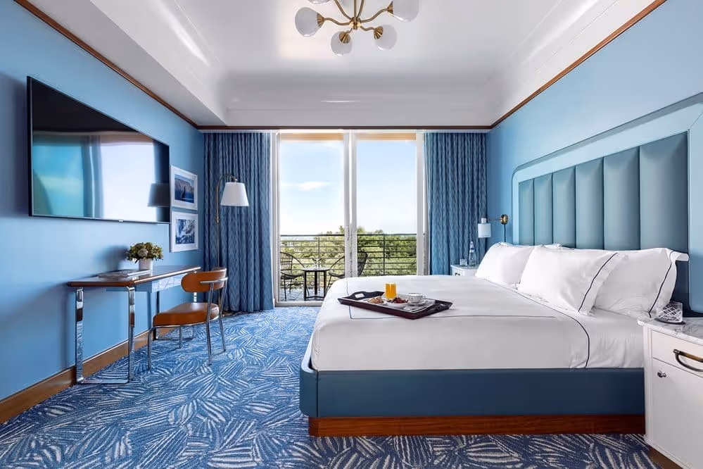 Vista do quarto com cama king-size, bandeja de café da manhã e varanda com vista para as árvores no Mr. C Miami – Coconut Grove, um hotel de luxo em Miami.