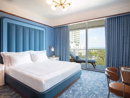 Quarto com cama king, varanda com vista e carpete geométrico azul. Mr. C Miami – Coconut Grove, um hotel de luxo em Miami.