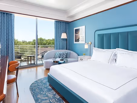 Quarto de hotel com cama king size, sofá, mesa de trabalho e varanda com vista para as árvores. Mr. C Miami – Coconut Grove, um hotel de luxo em Miami.
