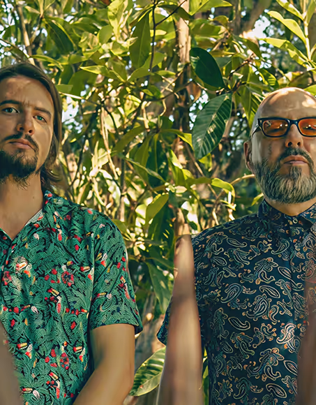 Two men in patterned shirts standing outdoors with leafy green trees in the background , Mr. C Miami – Coconut Grove, luxury hotel.