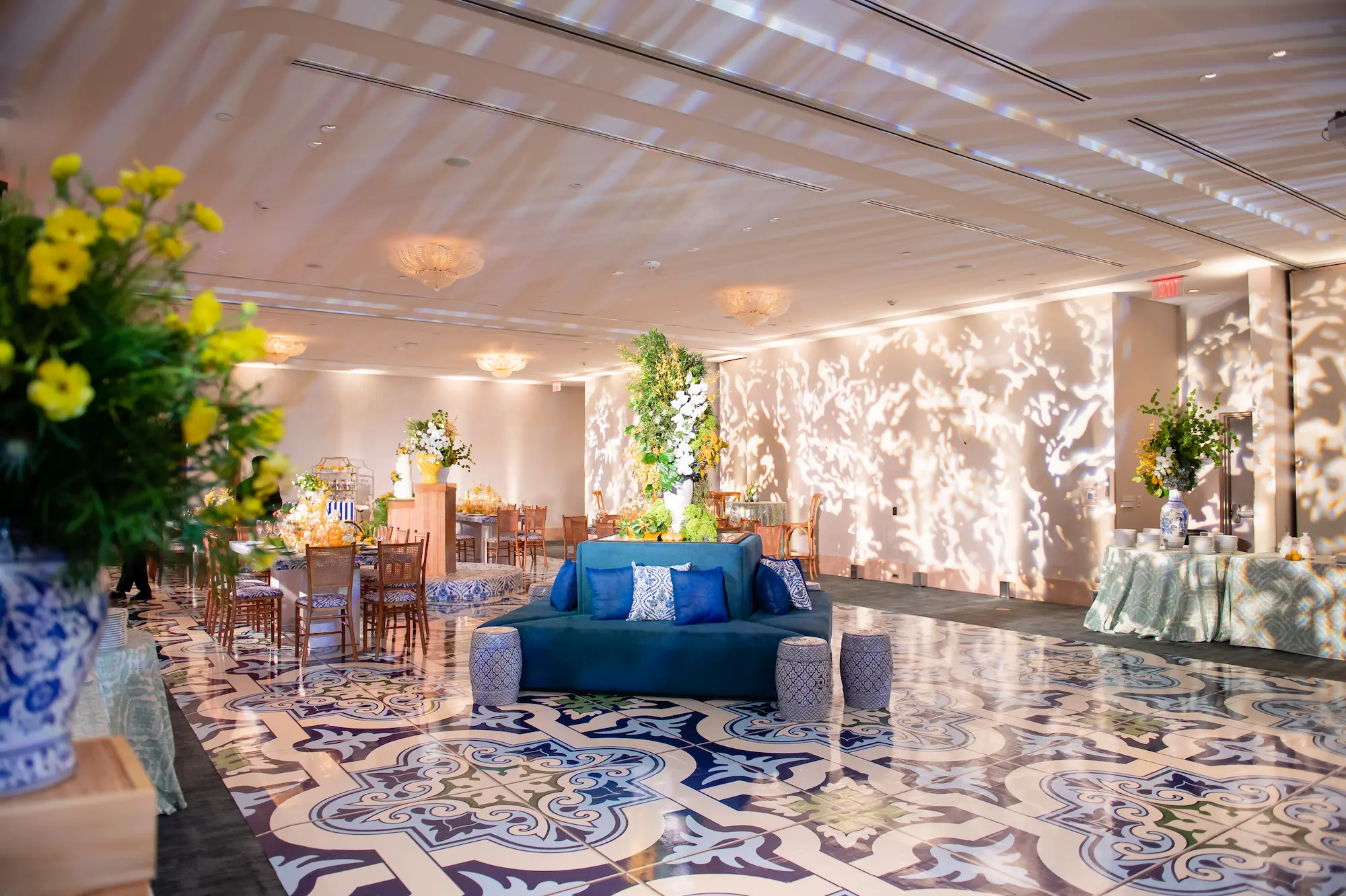 Opulent Starlight Ballroom foyer with a patterned carpet, blue sofa, and large floral arrangements. Mr. C Miami – Coconut Grove.