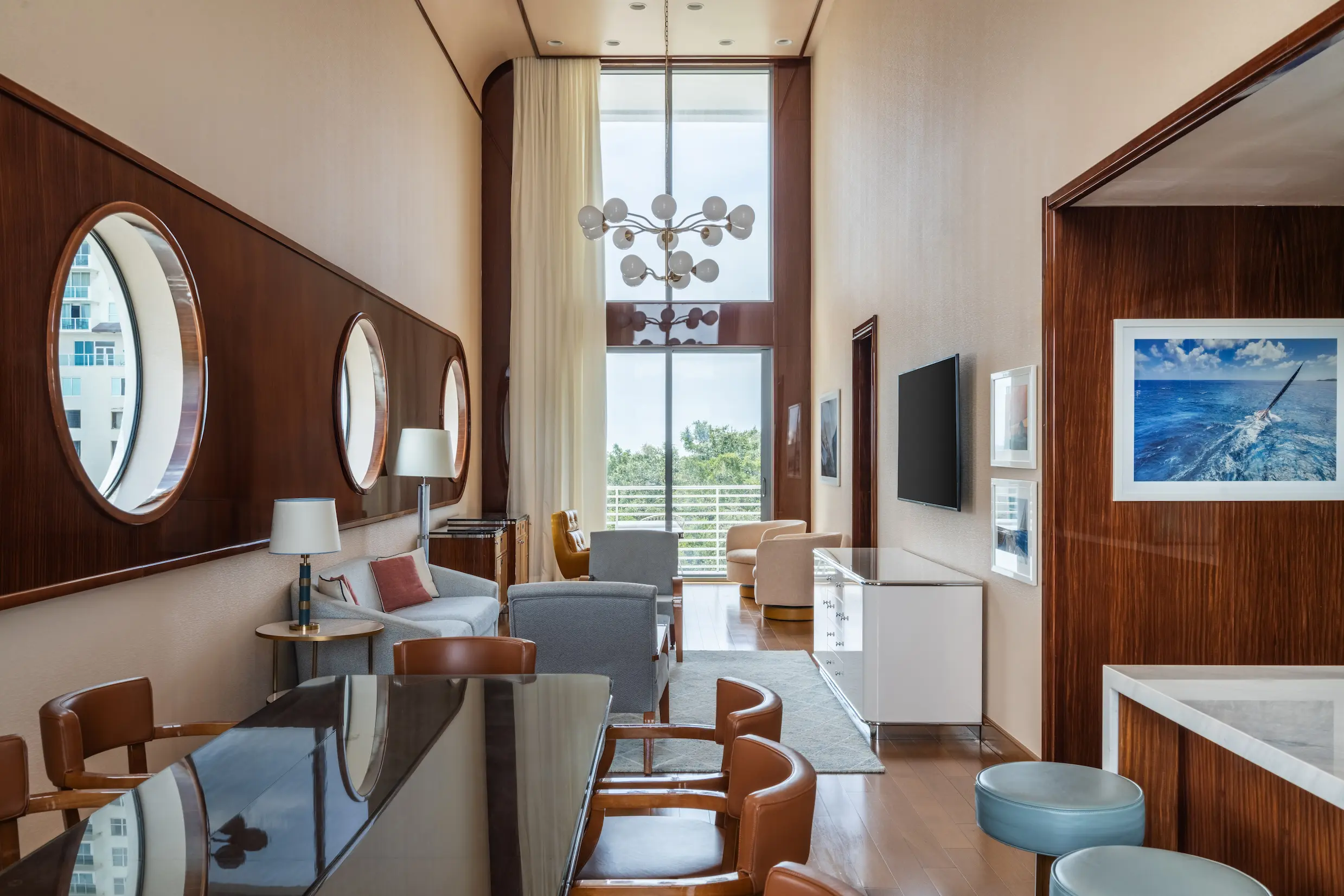 Modern living room with tall windows, round mirrors, chandelier, dining table, and seating area , Mr. C Miami – Coconut Grove, luxury hotel.