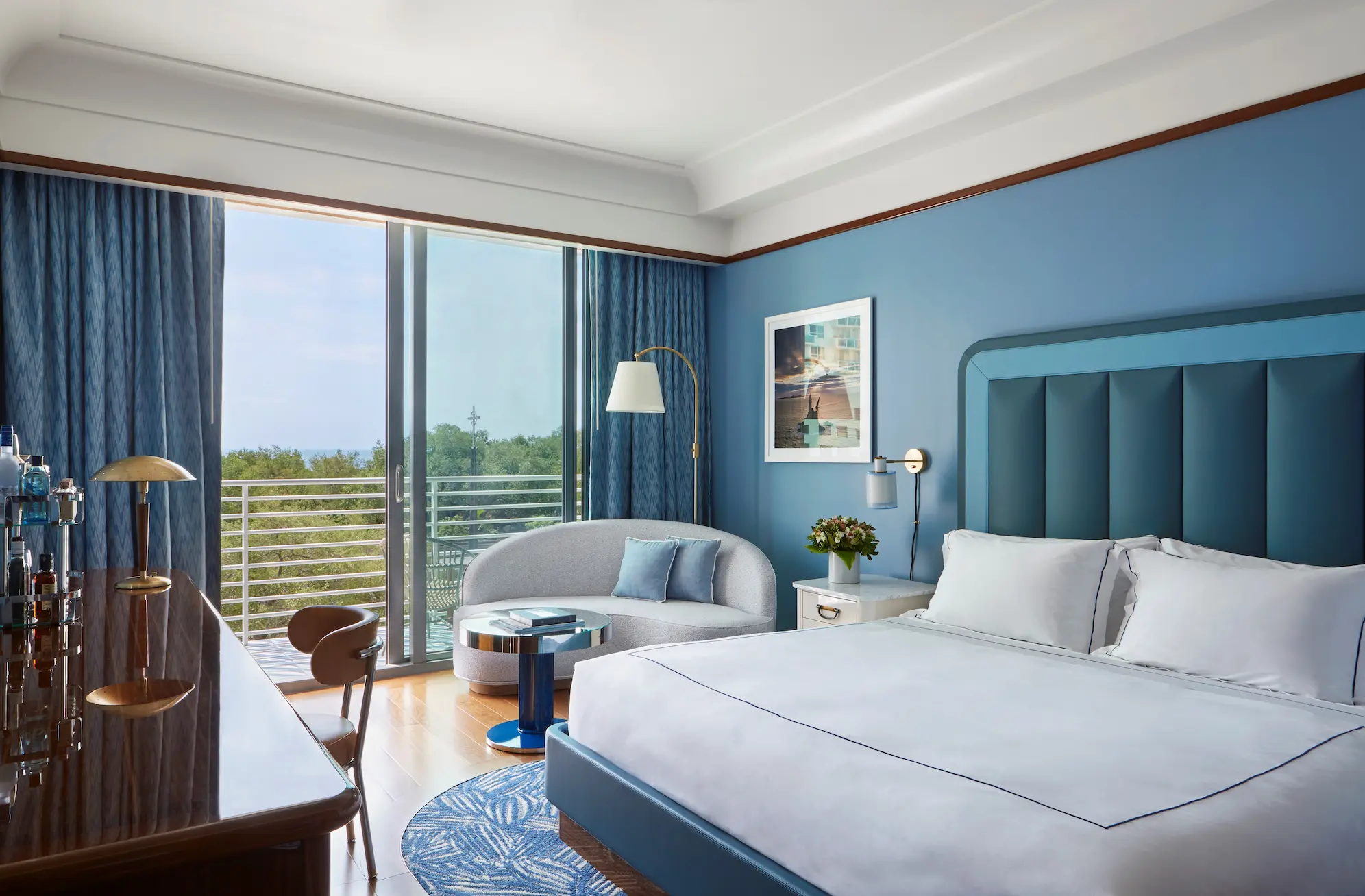 Vista ampla de um quarto azul no hotel Mr. C Miami – Coconut Grove, exibindo uma área de estar junto a uma janela grande.
