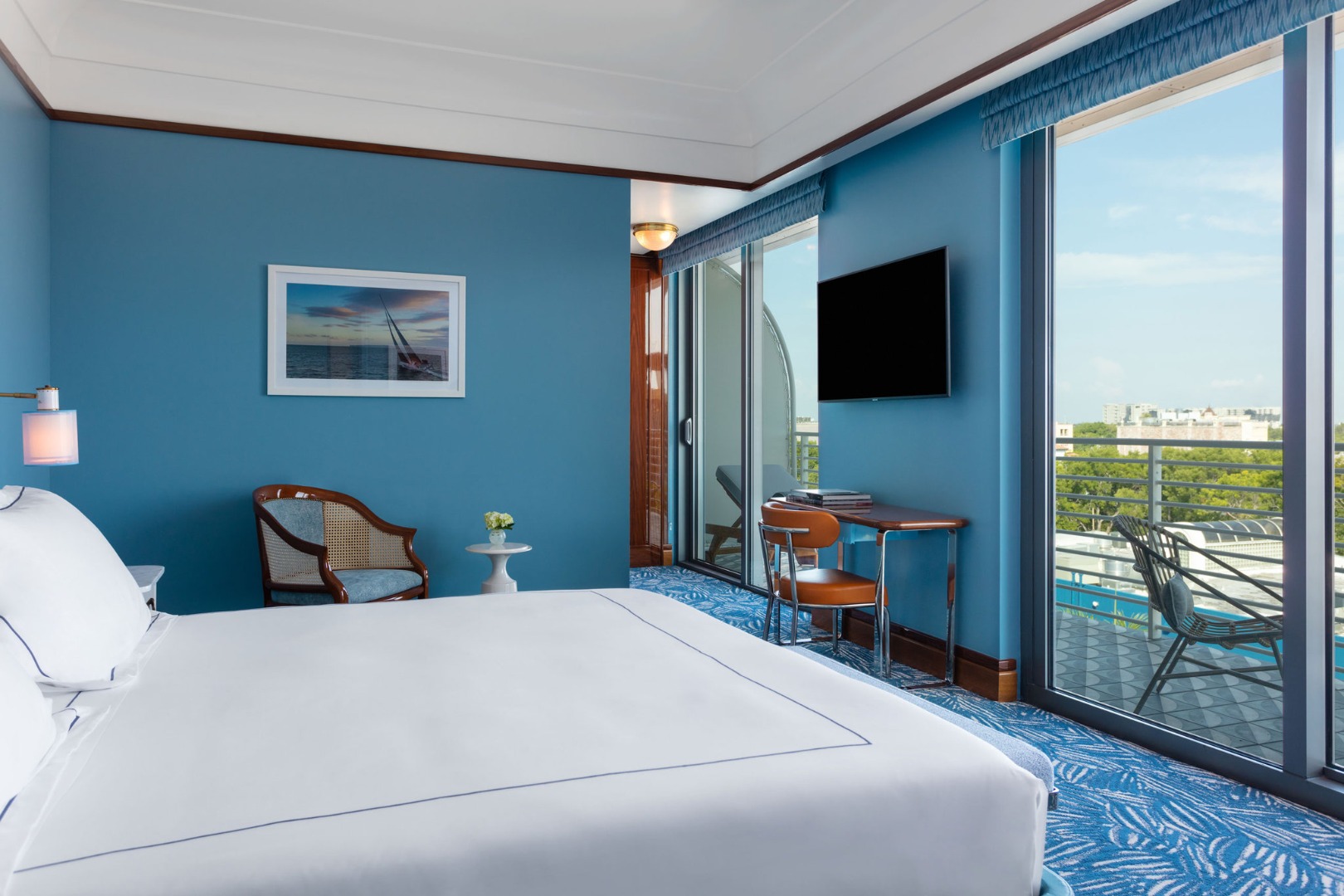 Cama king-size com parede azul e vista da cidade através das portas de vidro no Mr. C Miami – Coconut Grove, um hotel de luxo.