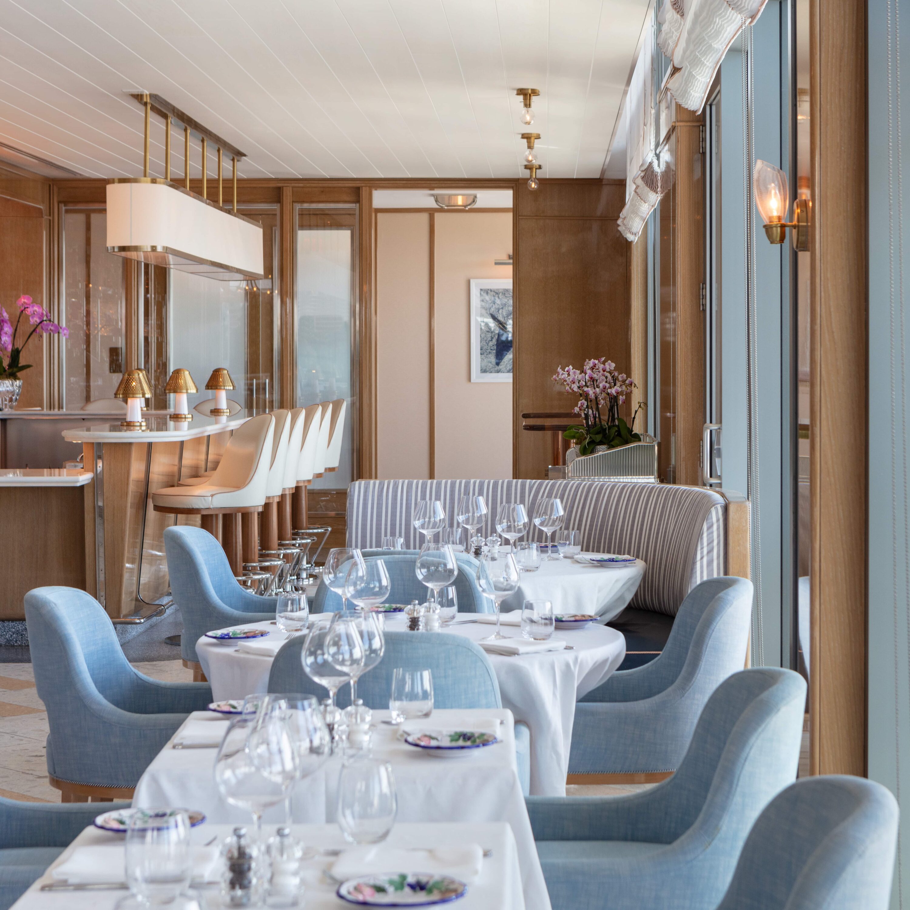 Salle de restaurant élégante avec chaises bleues, nappes blanches, verrerie et bar avec tabourets, Mr. C Miami – Coconut Grove, hôtel de luxe.