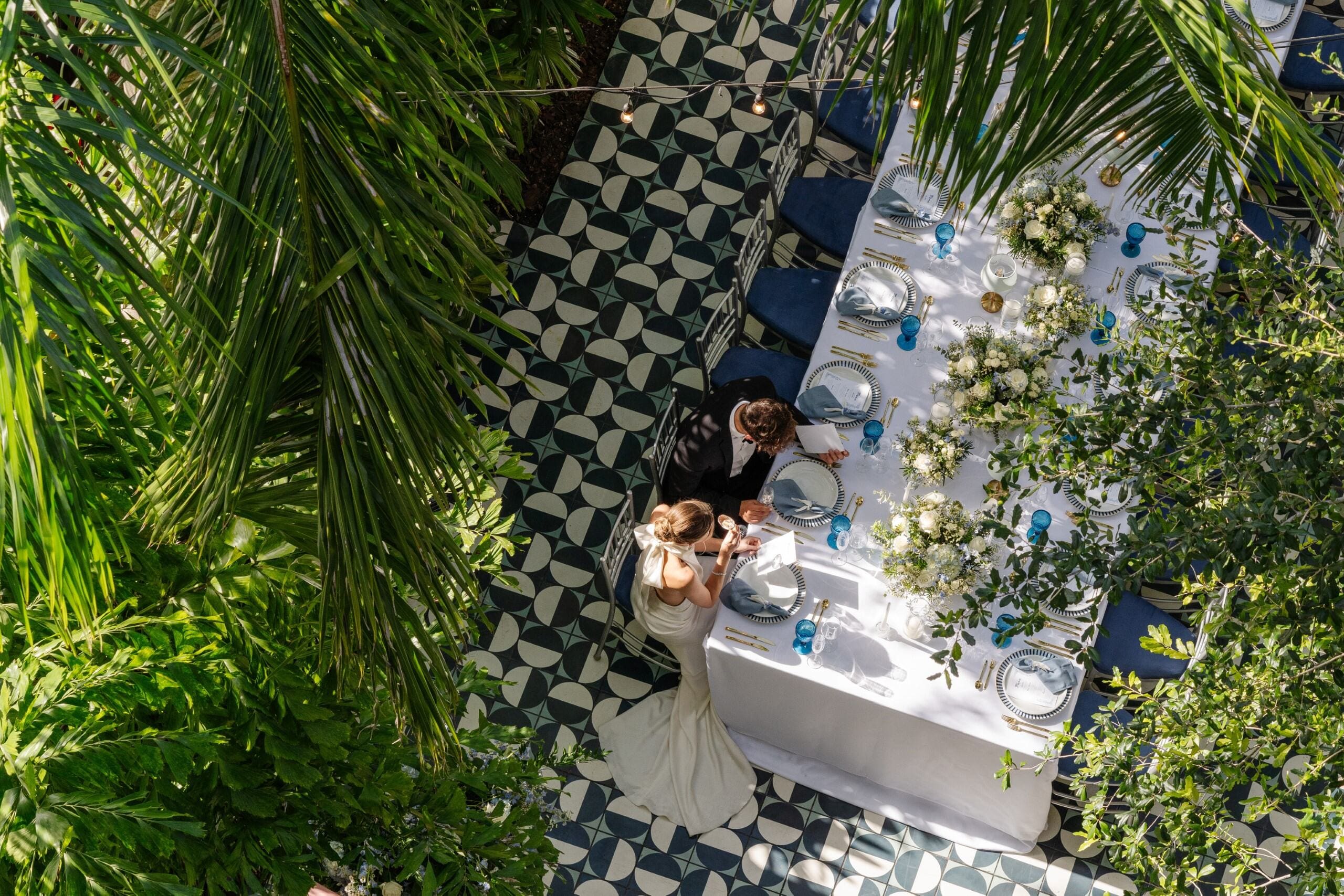 Overhead view of bride and groom seated at an outdoor wedding table with white linens and floral centerpieces , Mr. C Miami – Coconut Grove, luxury hotel.