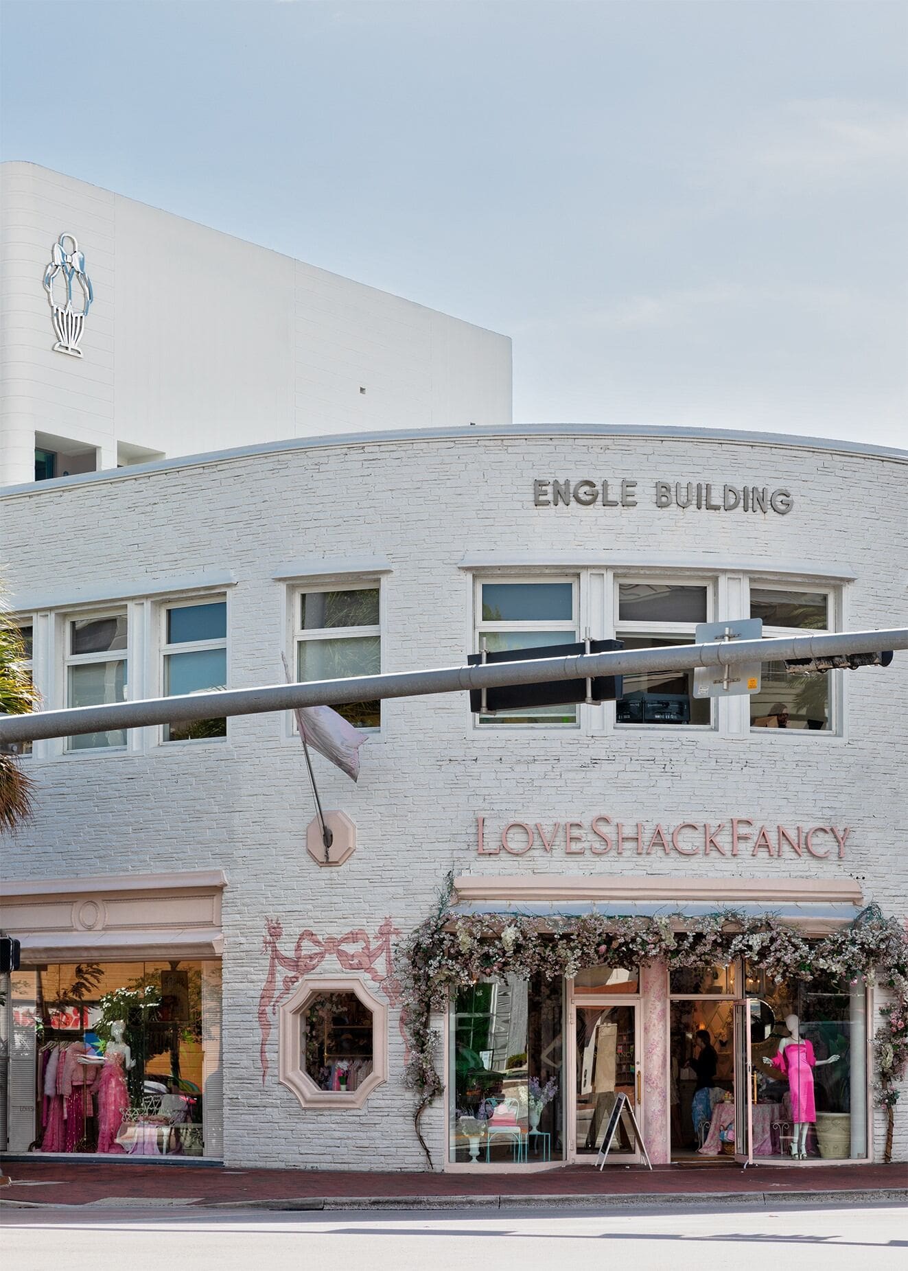 Façade en briques blanches de LoveShackFancy dans l'Engle Building avec décorations florales et mannequins en robes roses, Mr. C Miami – Coconut Grove, hôtel de luxe.