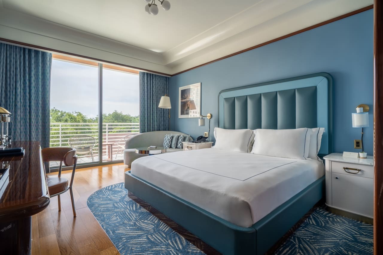 Camera d'albergo con letto king, testiera blu, pavimento in legno, tappeto blu, area salotto e balcone con sedie, Mr. C Miami – Coconut Grove, hotel di lusso.