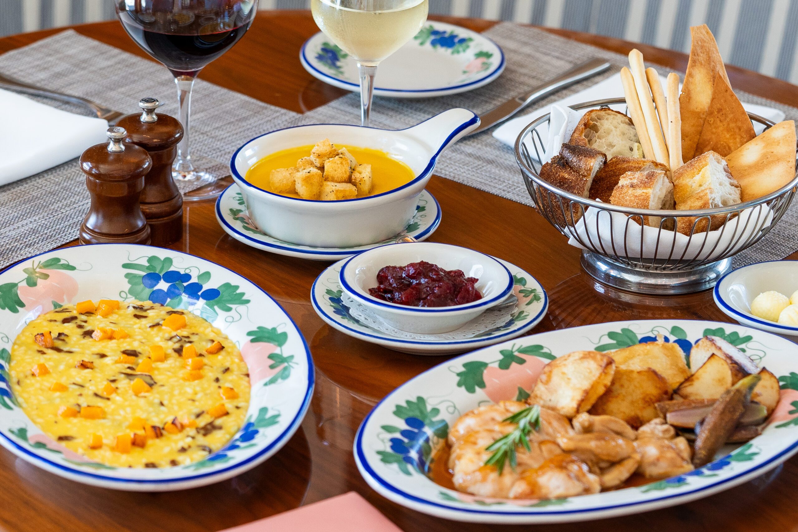 Allestimento tavola con piatti che includono risotto, gamberi con patate, zuppa, cestino del pane e due calici di vino, Mr. C Miami – Coconut Grove, hotel di lusso.