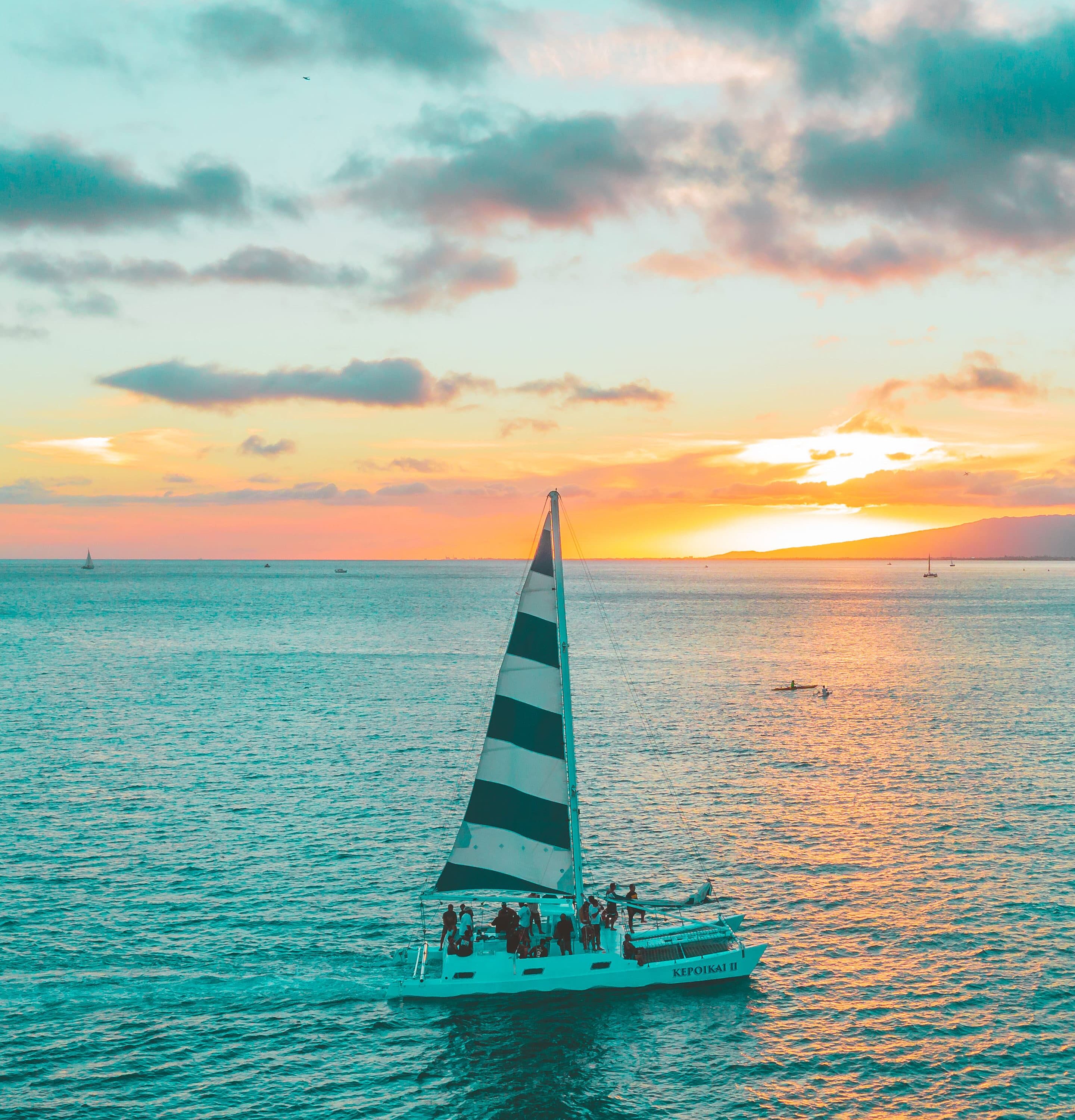 Barca a vela con vele a righe e passeggeri su acque calme durante un tramonto colorato, Mr. C Miami – Coconut Grove, hotel di lusso.