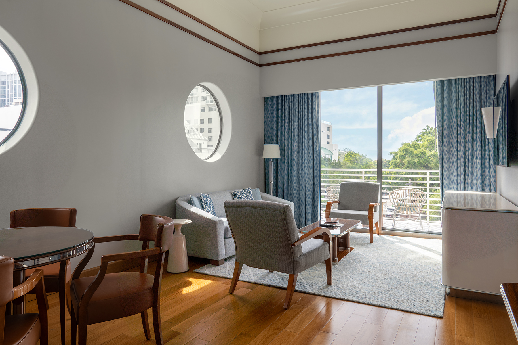 Sala de estar com móveis cinza, janela redonda e varanda. Mr. C Miami – Coconut Grove, um hotel de luxo em Miami.