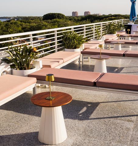 Terrazza lounge sul tetto con sedie a sdraio rosa e tavolini in legno al Mr C Coconut Grove, hotel di lusso nel sud della Florida