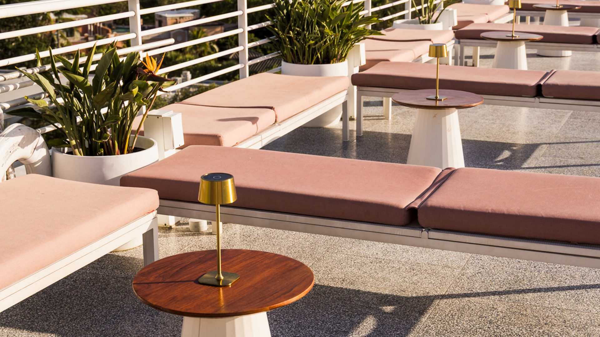 Sedie a sdraio rosa a bordo piscina e lampade da tavolo in ottone sulla terrazza panoramica del Mr C Coconut Grove, hotel di lusso nel sud della Florida
