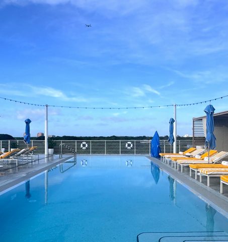 Piscina sul tetto con lettini a righe gialle e bianche sotto un cielo azzurro al Mr C Coconut Grove, hotel di lusso nel sud della Florida