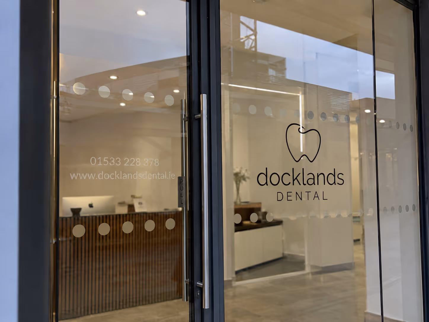 Glass doors of Docklands Dental office with logo, contact number, and website visible.