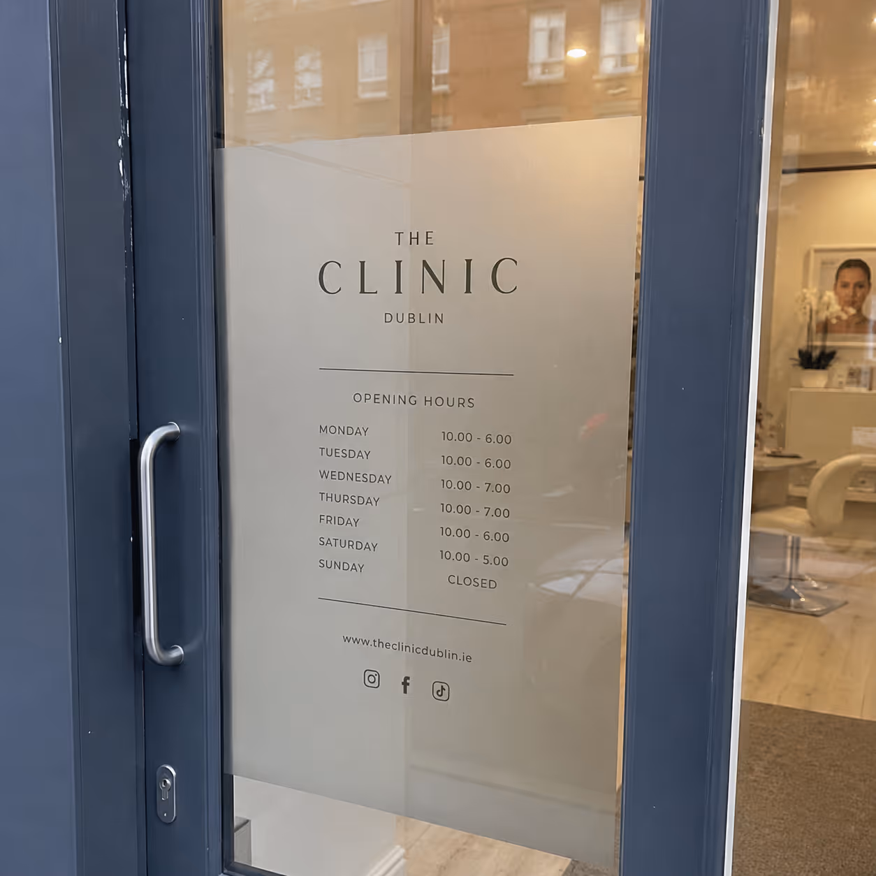 Glass door with The Clinic Dublin sign showing opening hours and social media icons.