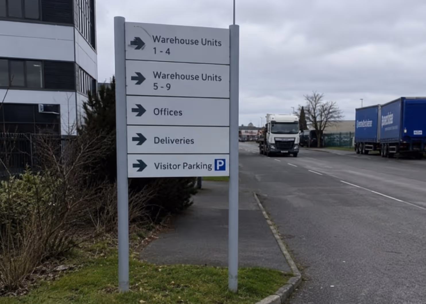 Directional sign showing arrows for warehouse units, offices, deliveries, and visitor parking on a roadside.