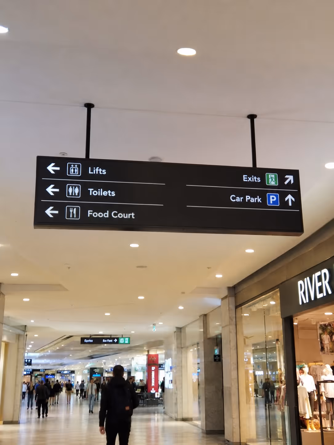 Mall overhead sign showing lifts, toilets, food court left; exits and car park right with icons.
