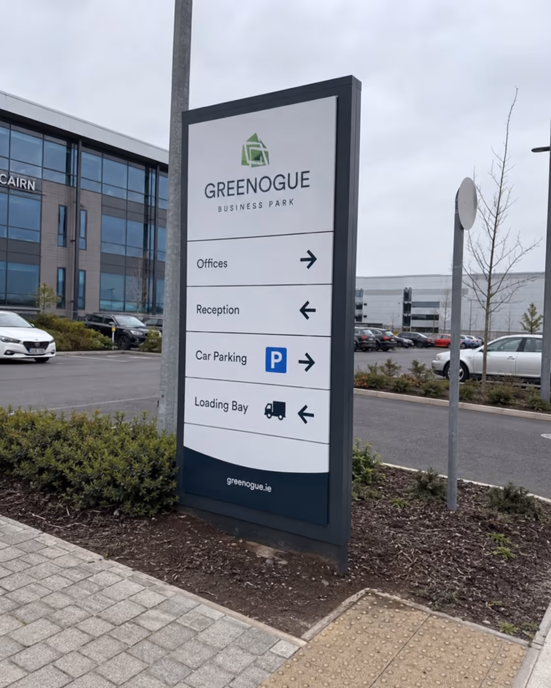 Greenogue Business Park sign directing to offices, reception, car parking, and loading bay with arrows.