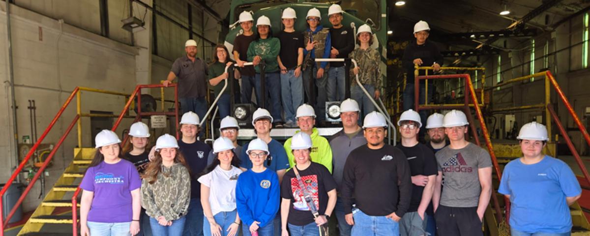 ATC welding students and a Paducah & Louisville Railway employee posing on scaffolding in front of a locomotive during a Power in Partnership field trip
