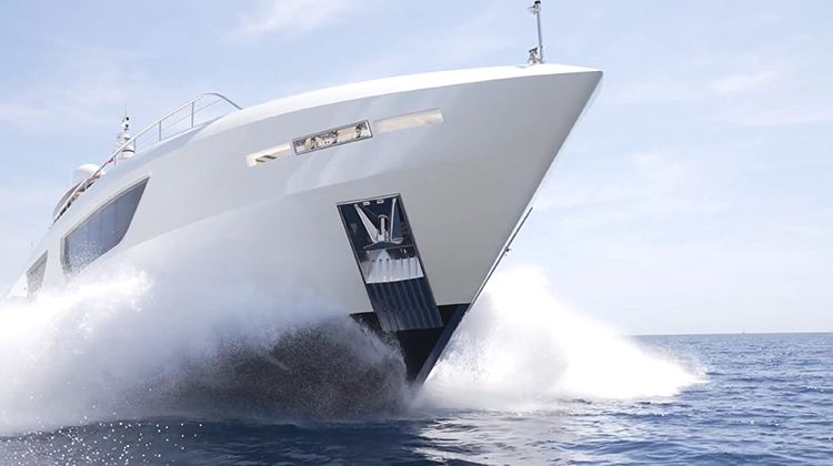 White yacht cutting through ocean water under a clear sky, creating splashes on both sides.