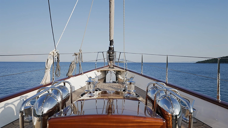 View from yacht's bow with polished wood and metal fittings on calm sea under clear sky.