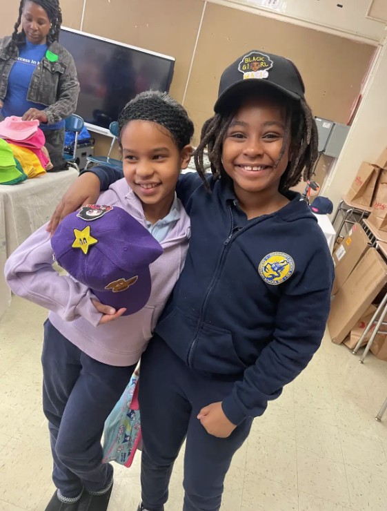 Two smiling students posing together at a school event holding hats