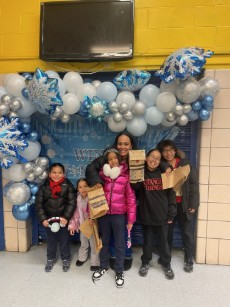 Students and adult posing with gifts at winter celebration backdrop