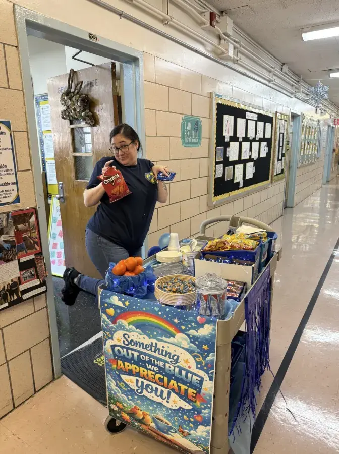 Staff member with appreciation cart full of snacks in school hallway