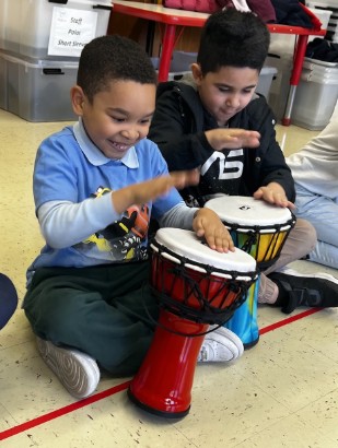 Two students playing djembe drums together during music class