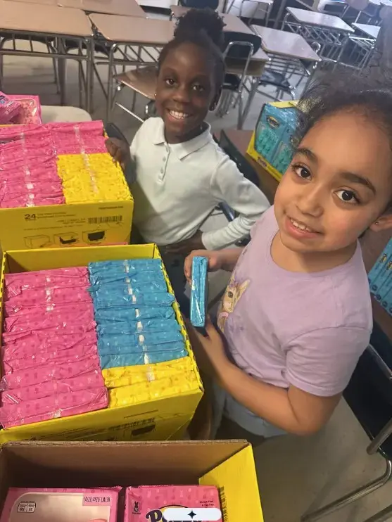 Two students smiling while sorting donated supplies in classroom