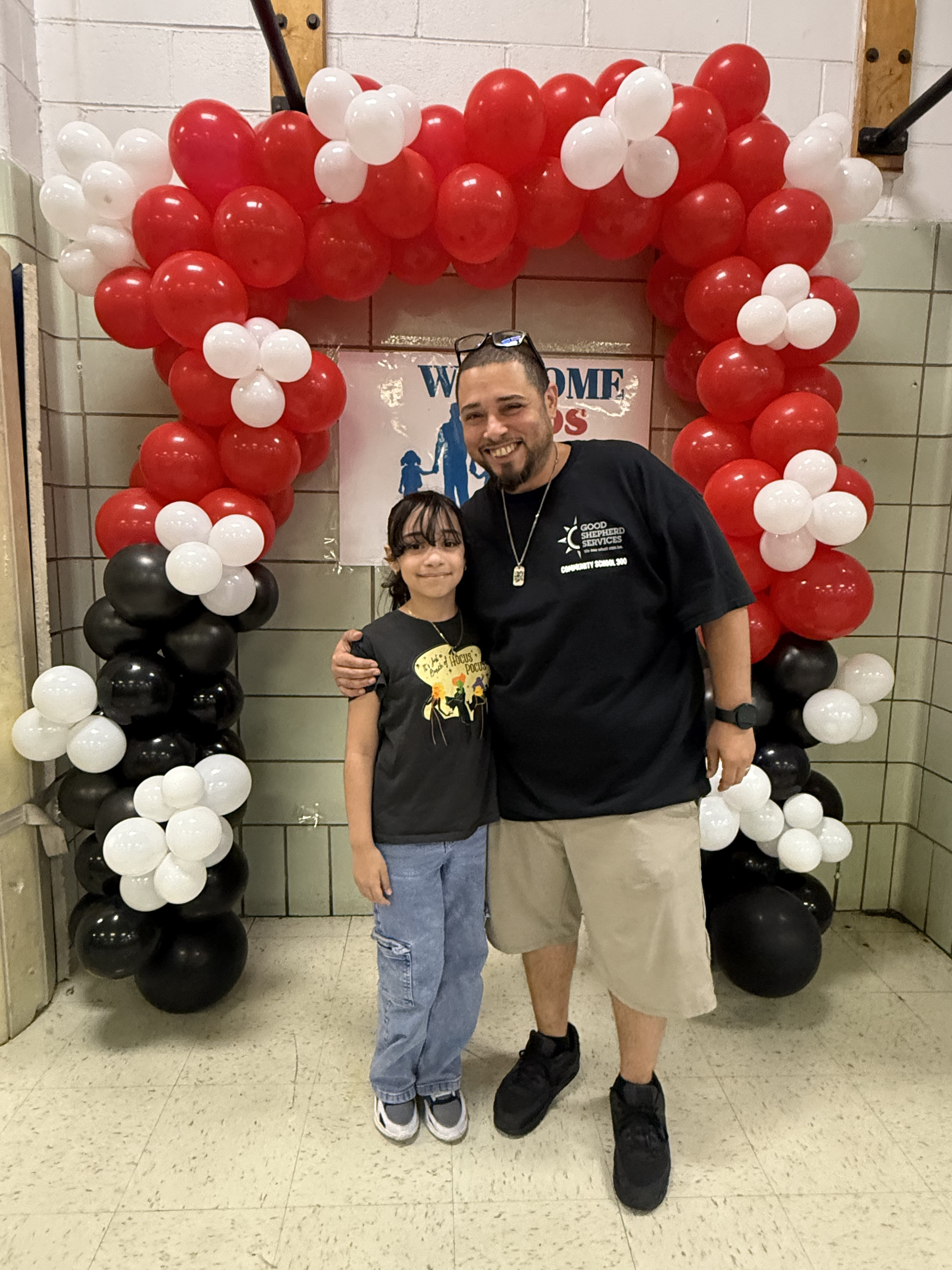 Adult and student posing under red white balloon arch at school welcome event